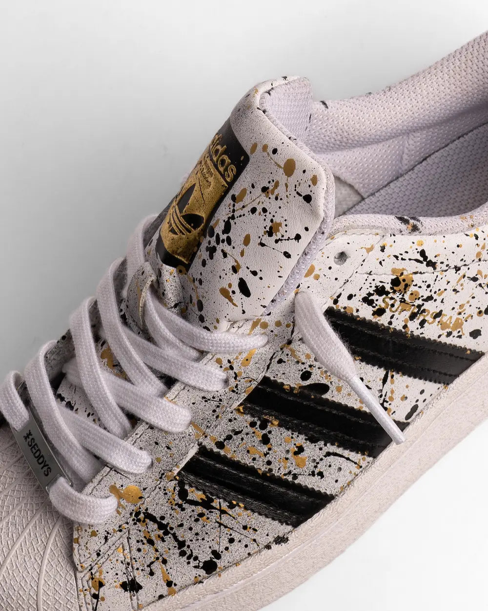 Adidas Superstar dipinta a mano con tecnica di schizzatura di colore nelle tonalità oro e nero